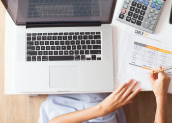 women writing next to the apple laptop with open accounting software