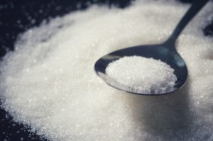 Sugar In Stainless Spoon On Some Sugar In Black Dish Background