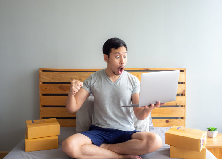 Surprise and shock face of Asian man success on making big sale of his online store. Concept of freelance startup and online business home office.