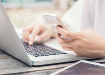 Female hands on laptop keyboard and holding smart phone, selective focus with shallow depth of field, soft vintage color tone