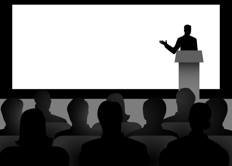 Silhouette illustration of man figure giving a speech on stage with blank big screen as the background