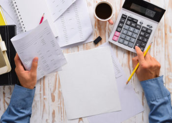 Top view businessmac use calculator and paper, cup of coffee, pencils and eraser on white wooden table.Concept for Financial accounting