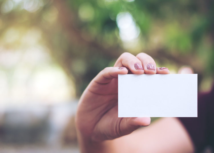 An image of a hand holding and showing empty business card with blur nature background