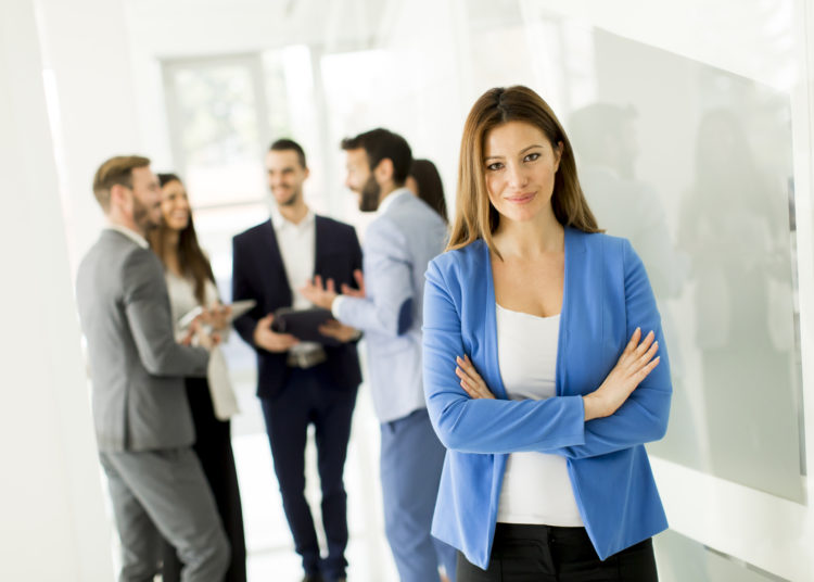 Young businesswoman posing while others young business people talking in the background