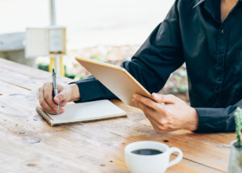 Business man hand holding tablet and writing notebook in coffee shop.