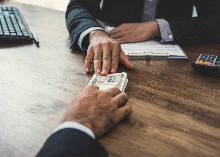 Businessman giving money, Japanese yen banknotes, to his partner at the table while making contract - loan, bribery and corruption concepts