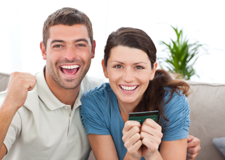 Portrait of a happy couple holding their credit card on the sofa at home