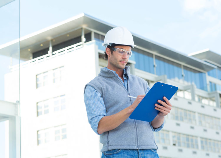 Male architect writing on clipboard outside building