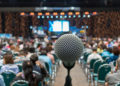 Microphone over the Abstract blurred photo of conference hall or seminar room in Exhibition Center background with Speakers on the stage and attendee background, Business meeting and education concept