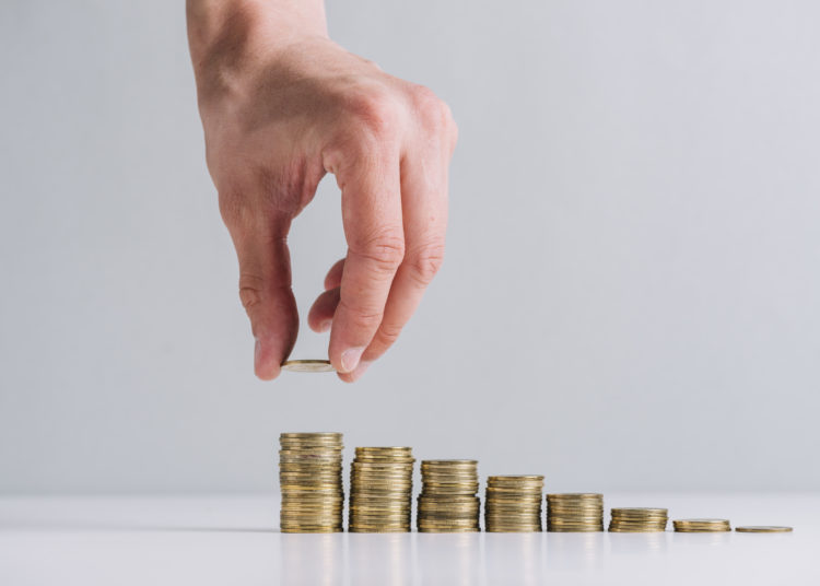 Human hand stacking golden coins on reflective desk