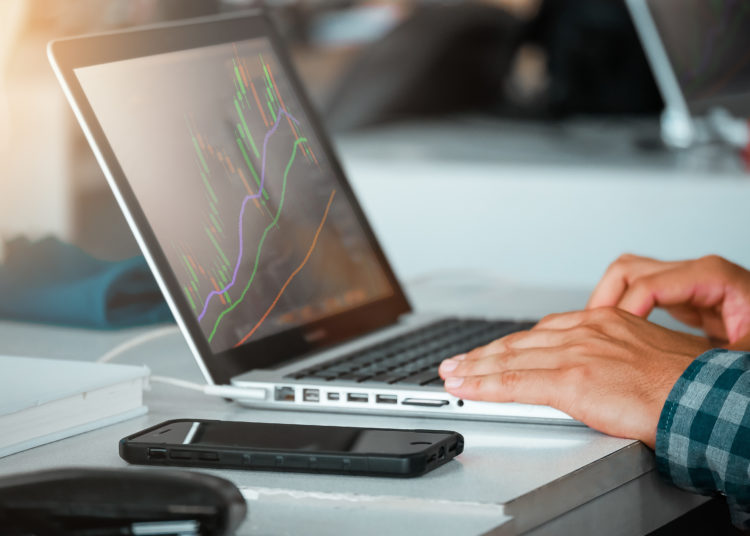 Close up of man using laptop for trading stock exchange market in coffee cafe