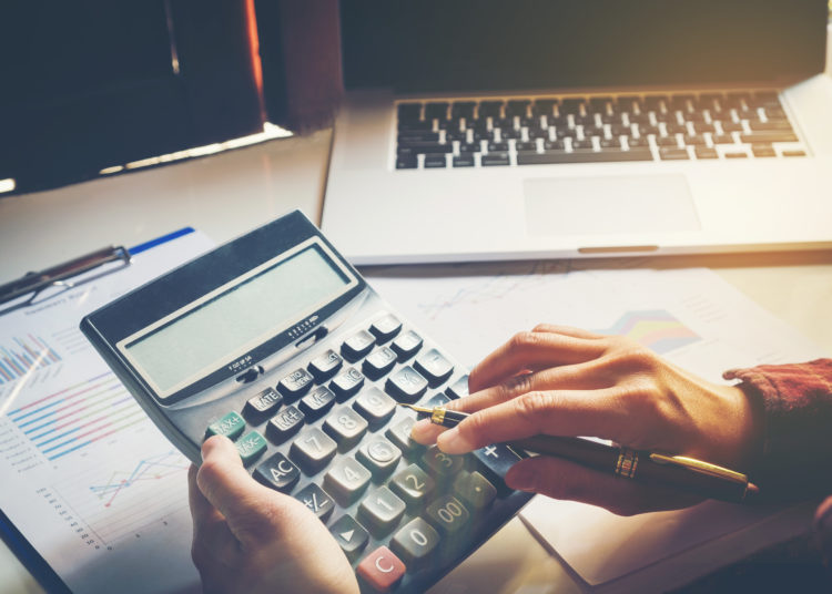 Businessman's hands with calculator and using laptop at the office and Financial data analyzing counting on wood desk