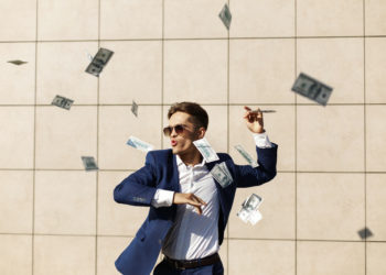 Young businessman throughs around dollars and dances on the street