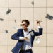 Young businessman throughs around dollars and dances on the street