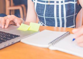 Woman hand working at a computer and writing on a notepad with a pen in the office.Web banner.