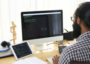 IT technician sitting by workplace in front of computer screen, analyzing data or creating new code or language